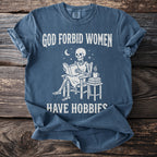 Blue t-shirt with skeleton reading a book and text: God forbid women have hobbies.