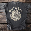 Dark grey t-shirt with "Keep The North" and a circular design of a fox, bird, and pine cones.