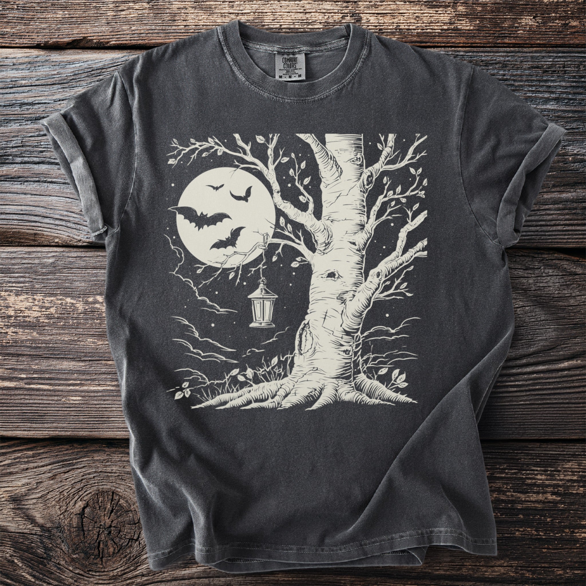 Dark t-shirt with a cream graphic of a tree, full moon, bats, and a lantern.