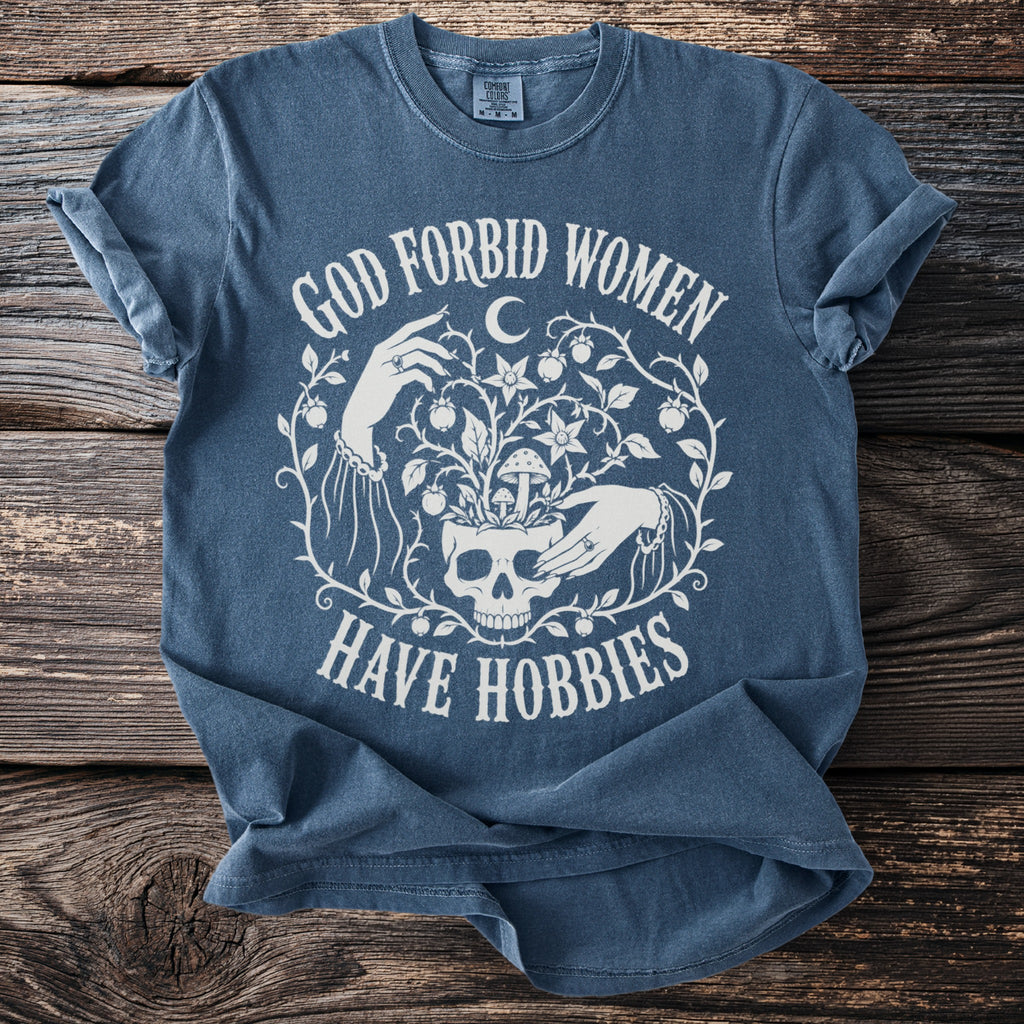 Blue t-shirt with white text and skull graphic saying "God Forbid Women Have Hobbies".