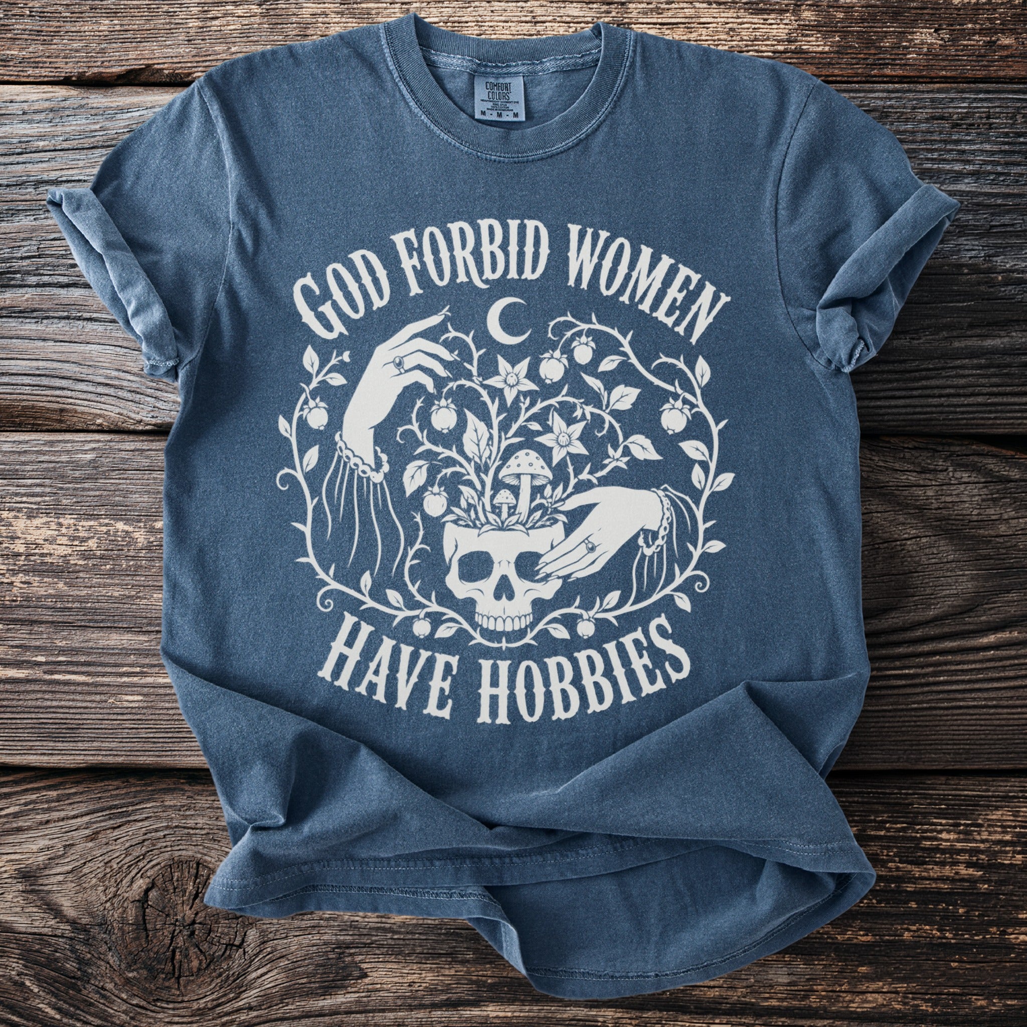 Blue t-shirt with white text and skull graphic saying "God Forbid Women Have Hobbies".