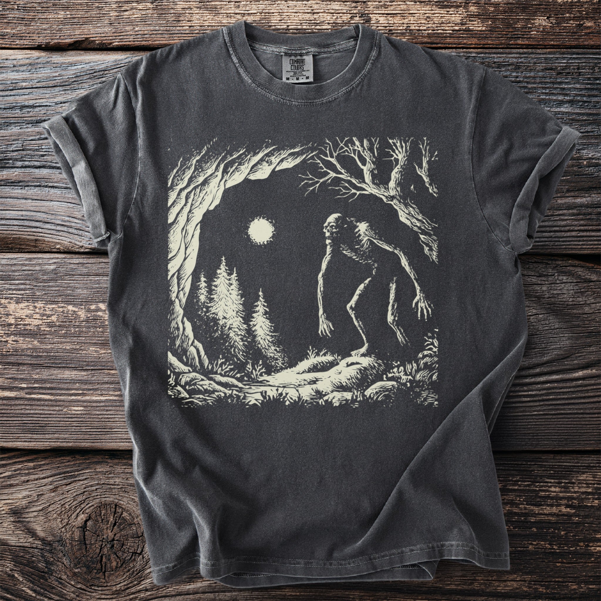 Dark t-shirt with a graphic of a creature in a forest under moonlight.