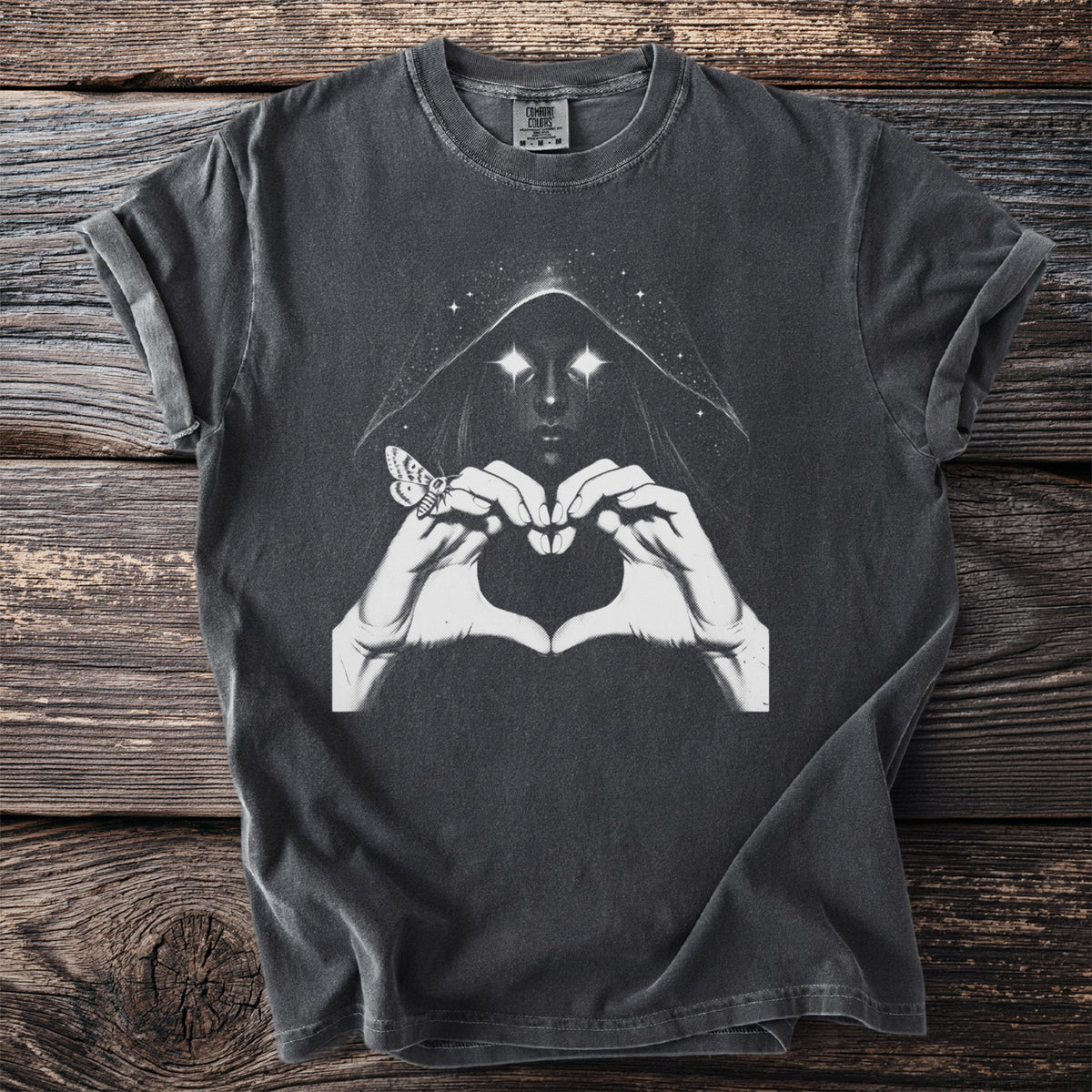 Dark t-shirt with a hooded figure, glowing eyes, hands forming a heart, and a moth.