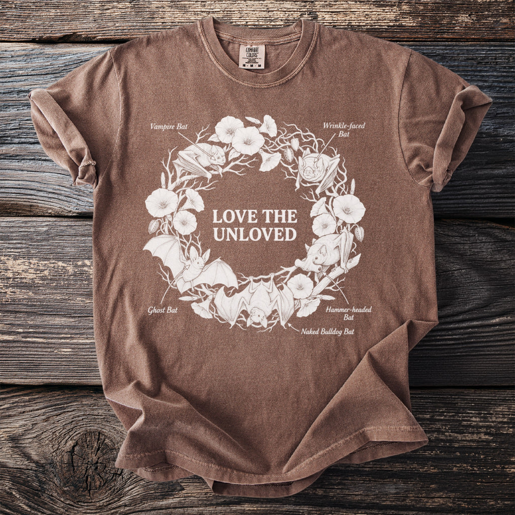 Brown t-shirt with white illustration of bats, flowers, and text "LOVE THE UNLOVED".