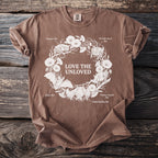 Brown t-shirt with white illustration of bats, flowers, and text "LOVE THE UNLOVED".