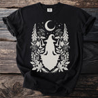 Black t-shirt with a cream graphic of a meditating witch, crescent moon, stars, and botanical elements.