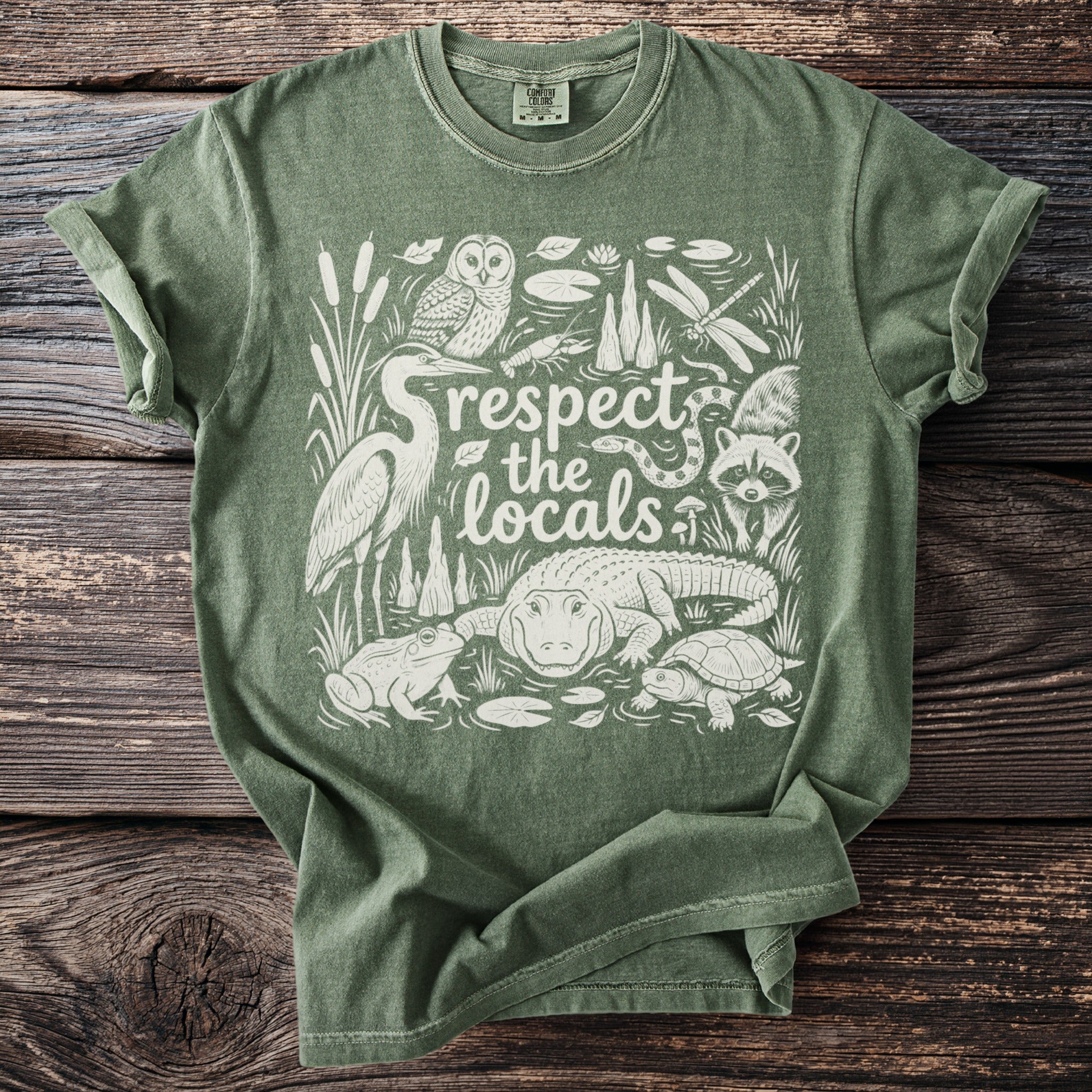 Green t-shirt with white line art of swamp animals and text "respect the locals."