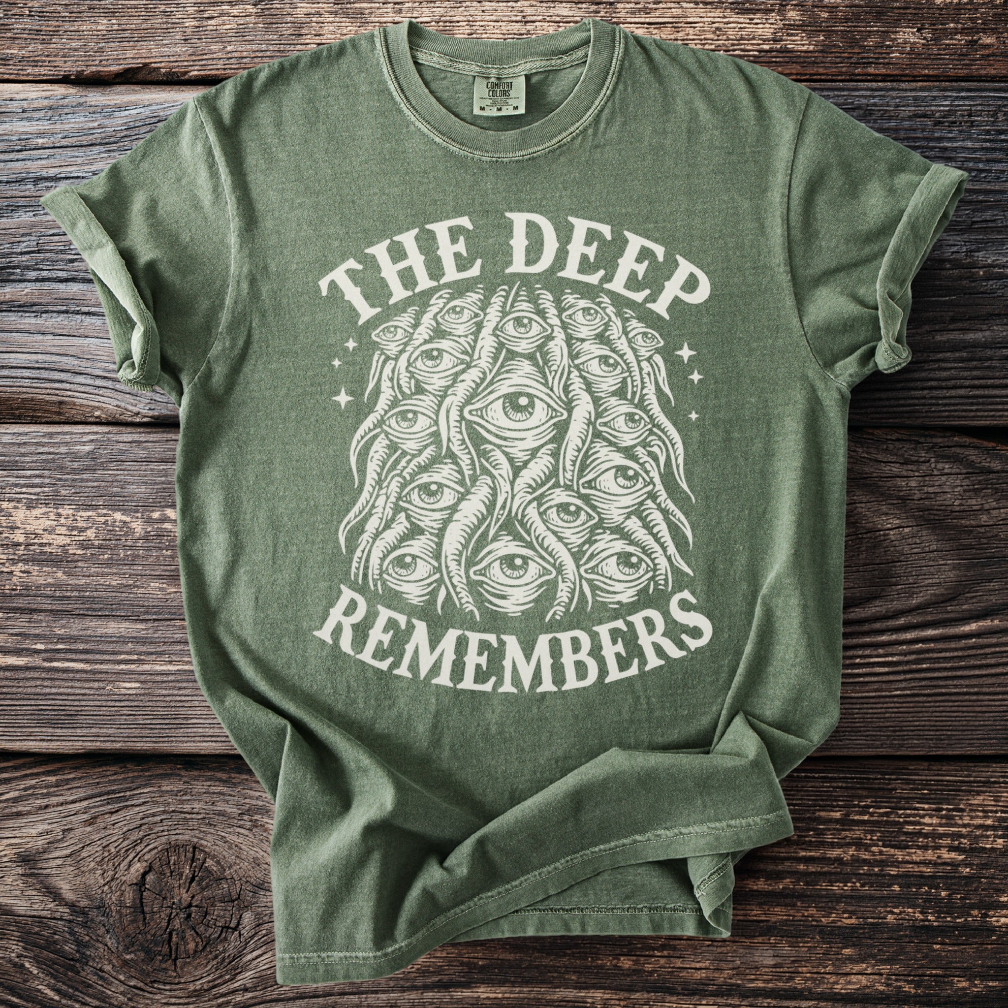Green t-shirt with white text "THE DEEP REMEMBERS" and an illustration of many eyes.