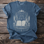 Blue t-shirt with a mystical black cat, moon phases, candles, and an open book.