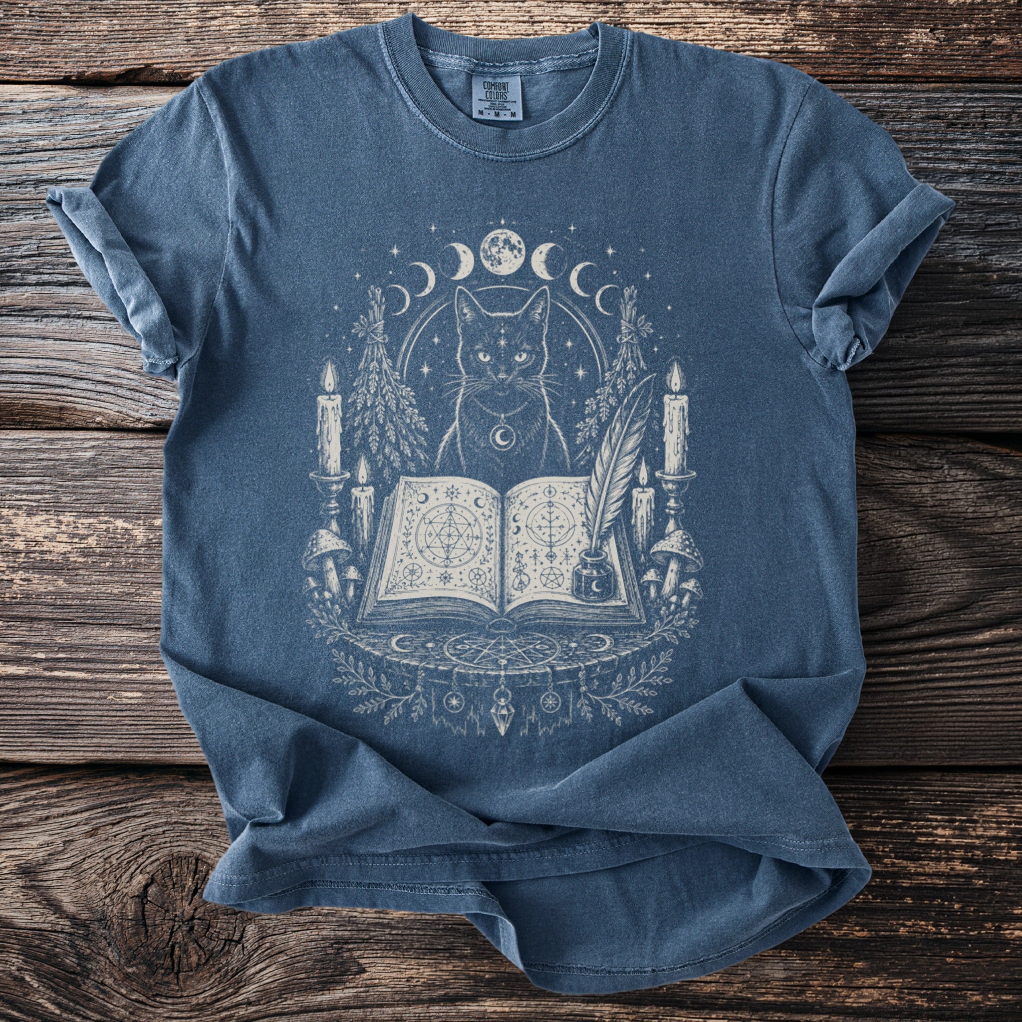 Blue t-shirt with a mystical black cat, moon phases, candles, and an open book.