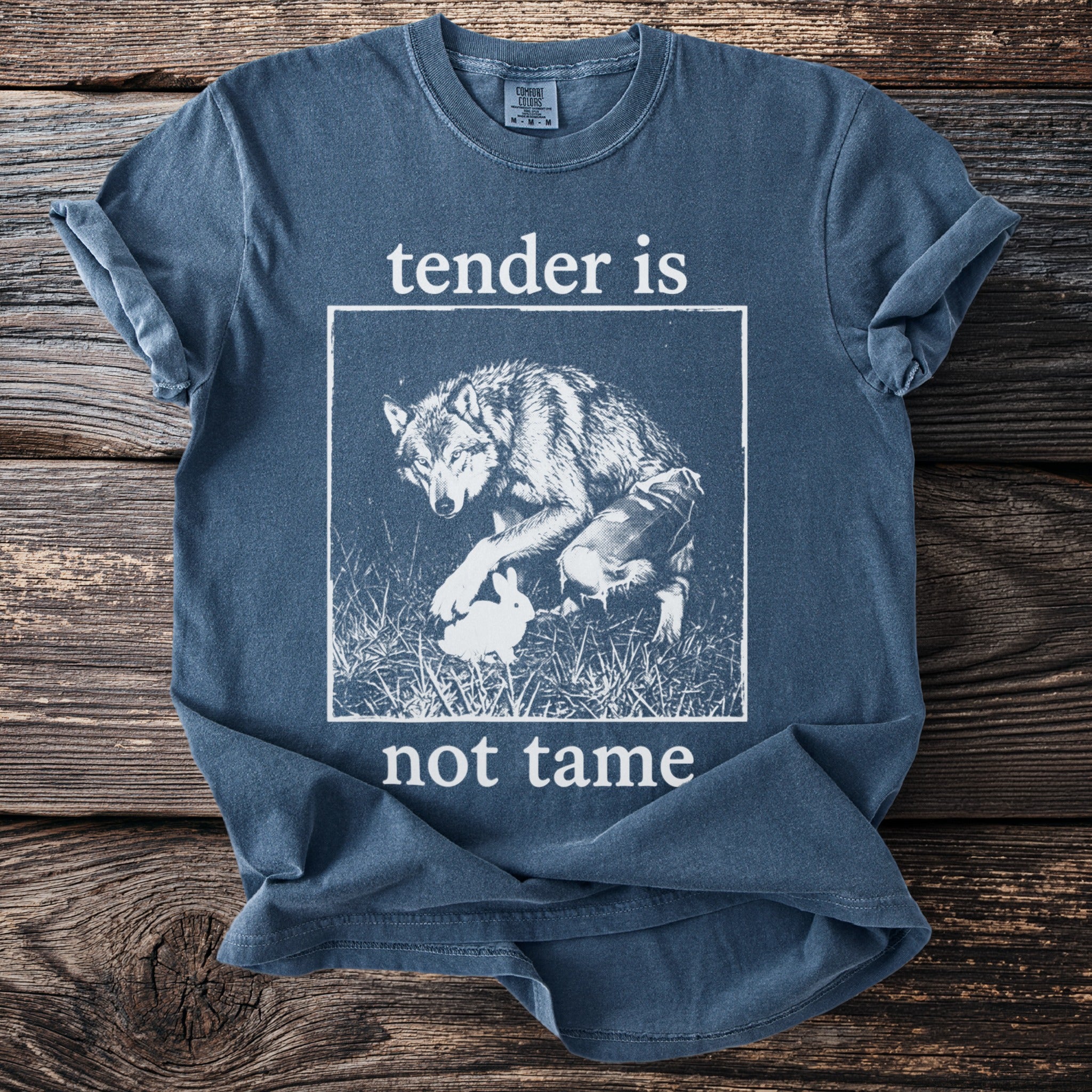 Blue t-shirt with wolf and rabbit graphic and text "tender is not tame."