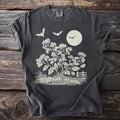Dark t-shirt with a cream graphic of bats, moon, flowering plant, and fence.