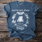 Blue t-shirt with a circular design of bugs and insects surrounding a frog, reading "you're not alone there are bugs".