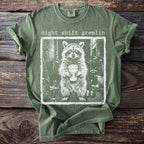 Green t-shirt with a distressed graphic of a raccoon holding a coffee cup with text "night shift gremlin".