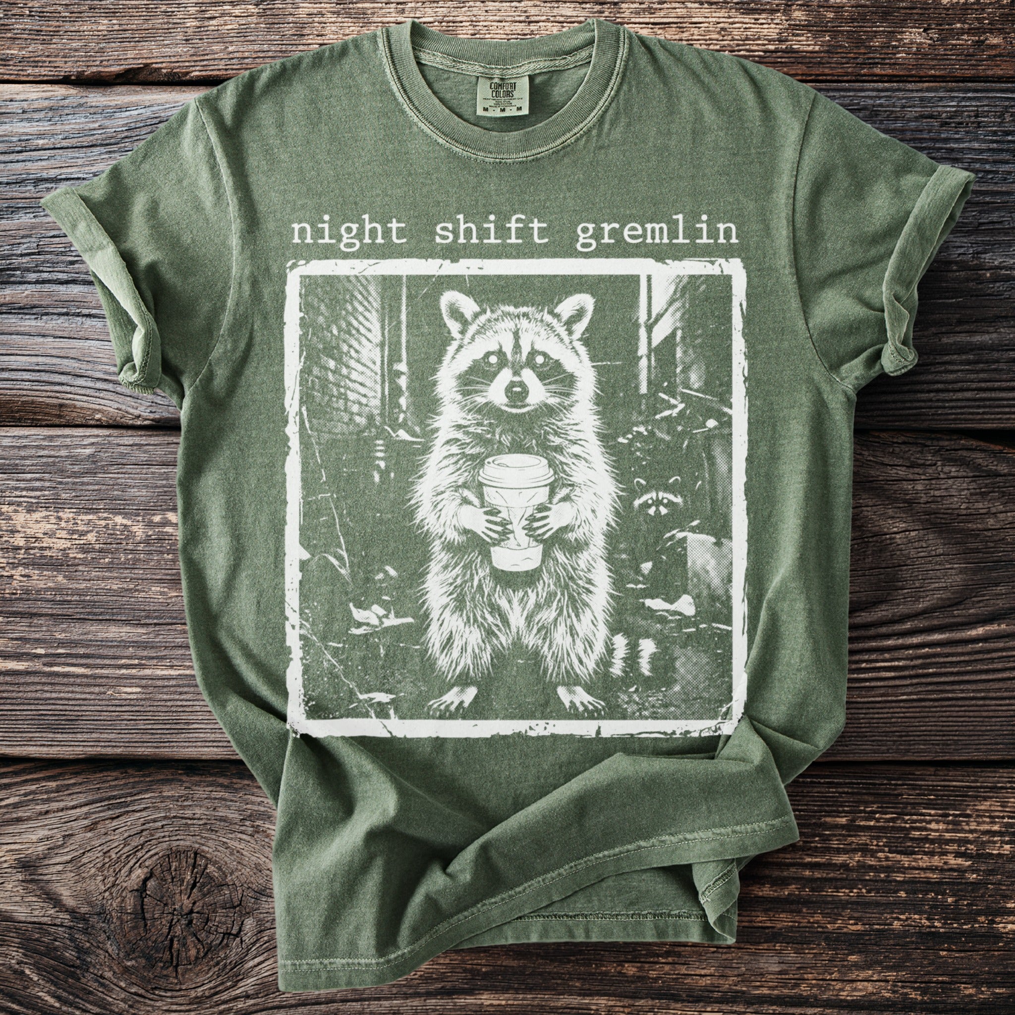 Green t-shirt with a distressed graphic of a raccoon holding a coffee cup with text "night shift gremlin".