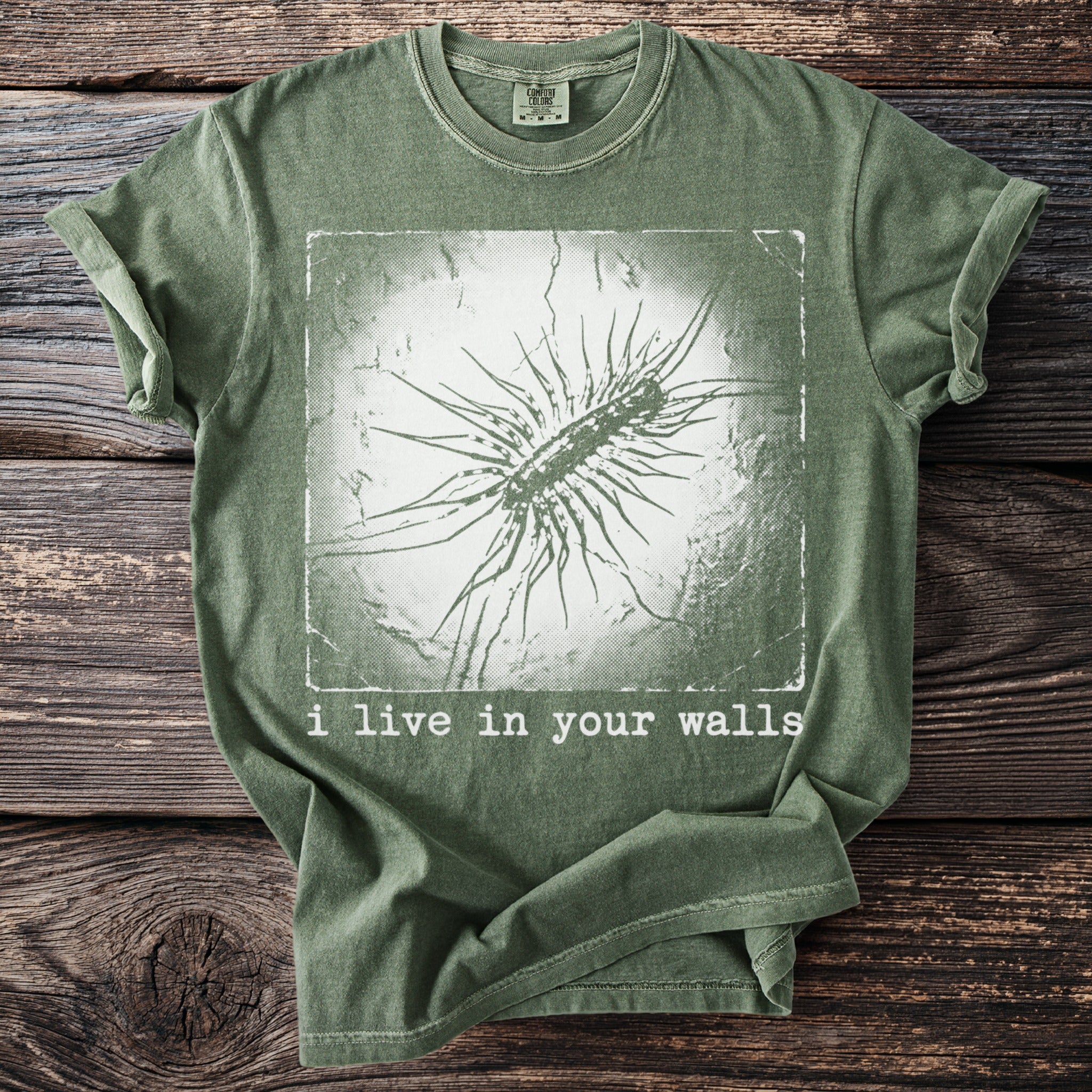 Green t-shirt with graphical print and text "i live in your walls."