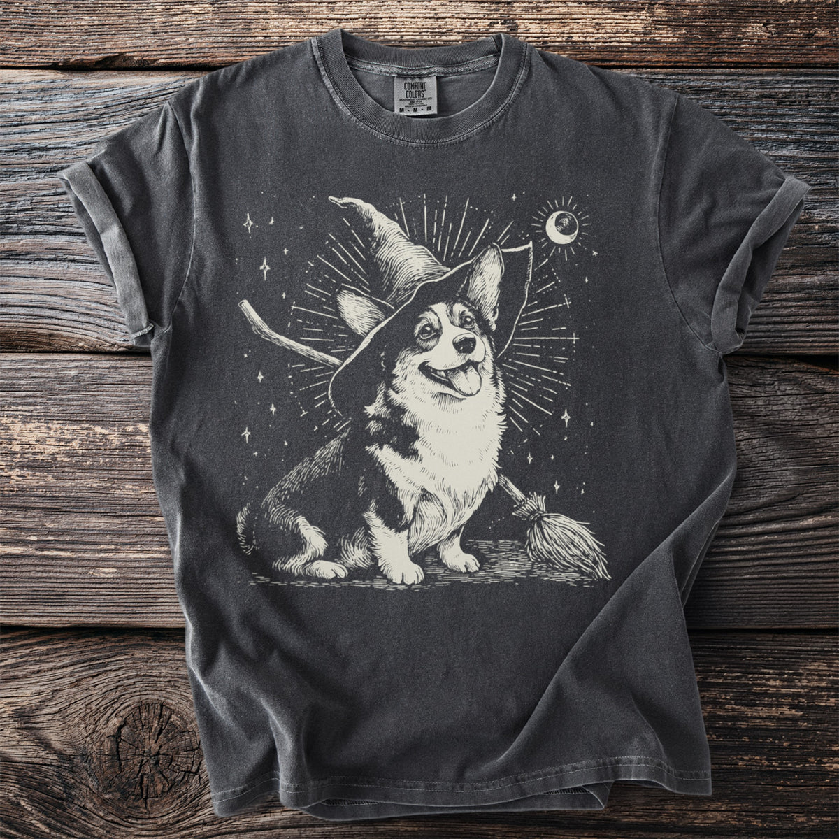 Corgi wearing a witch hat with a broom and moon graphic on a dark t-shirt.