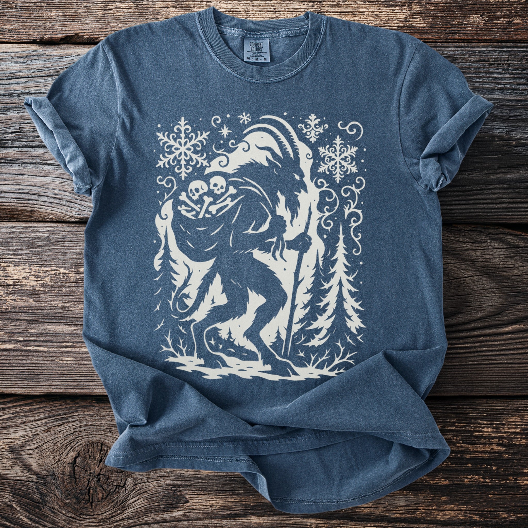 Blue t-shirt with white graphic of Krampus surrounded by snowflakes and trees.