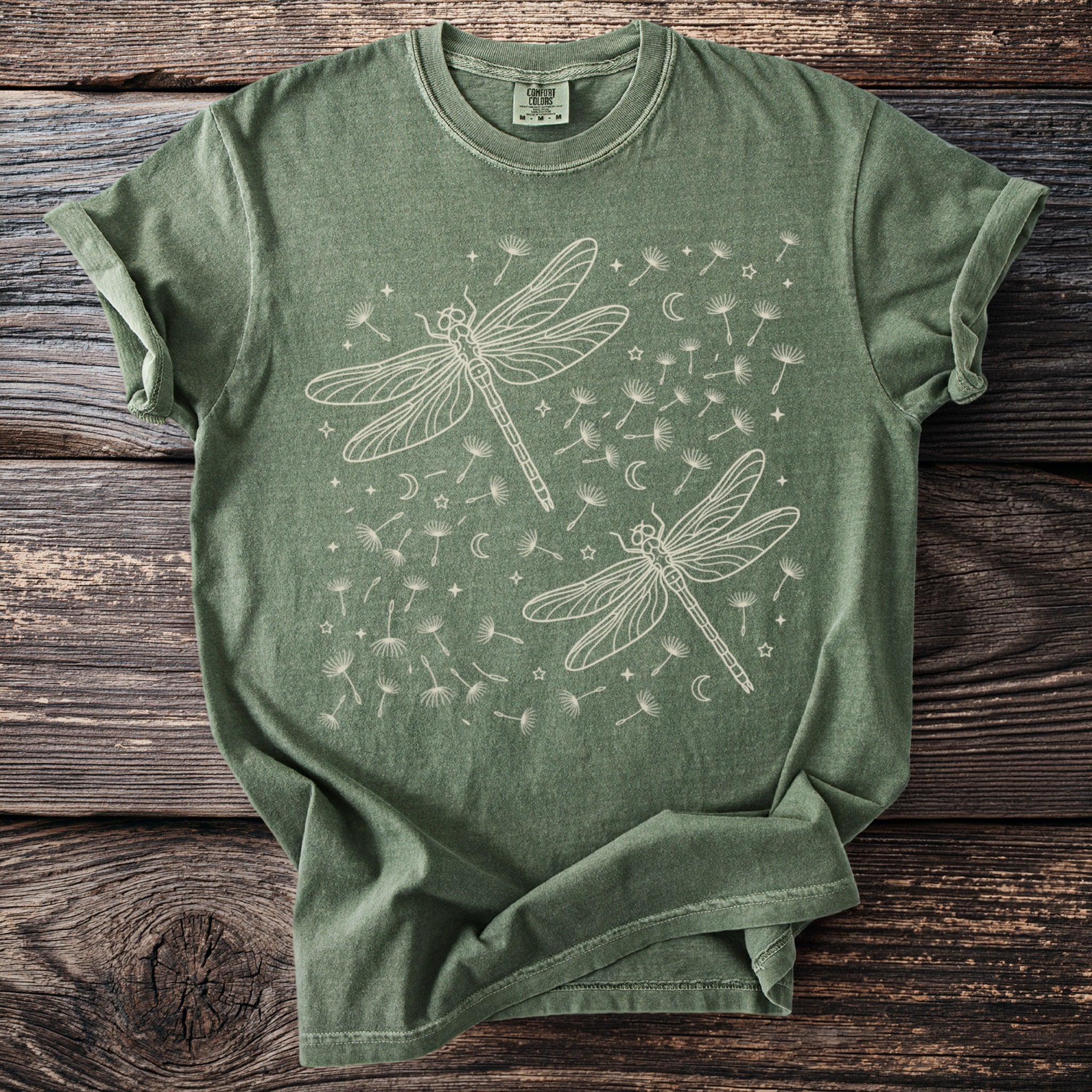 Green t-shirt with two outline dragonflies and dandelion seeds.
