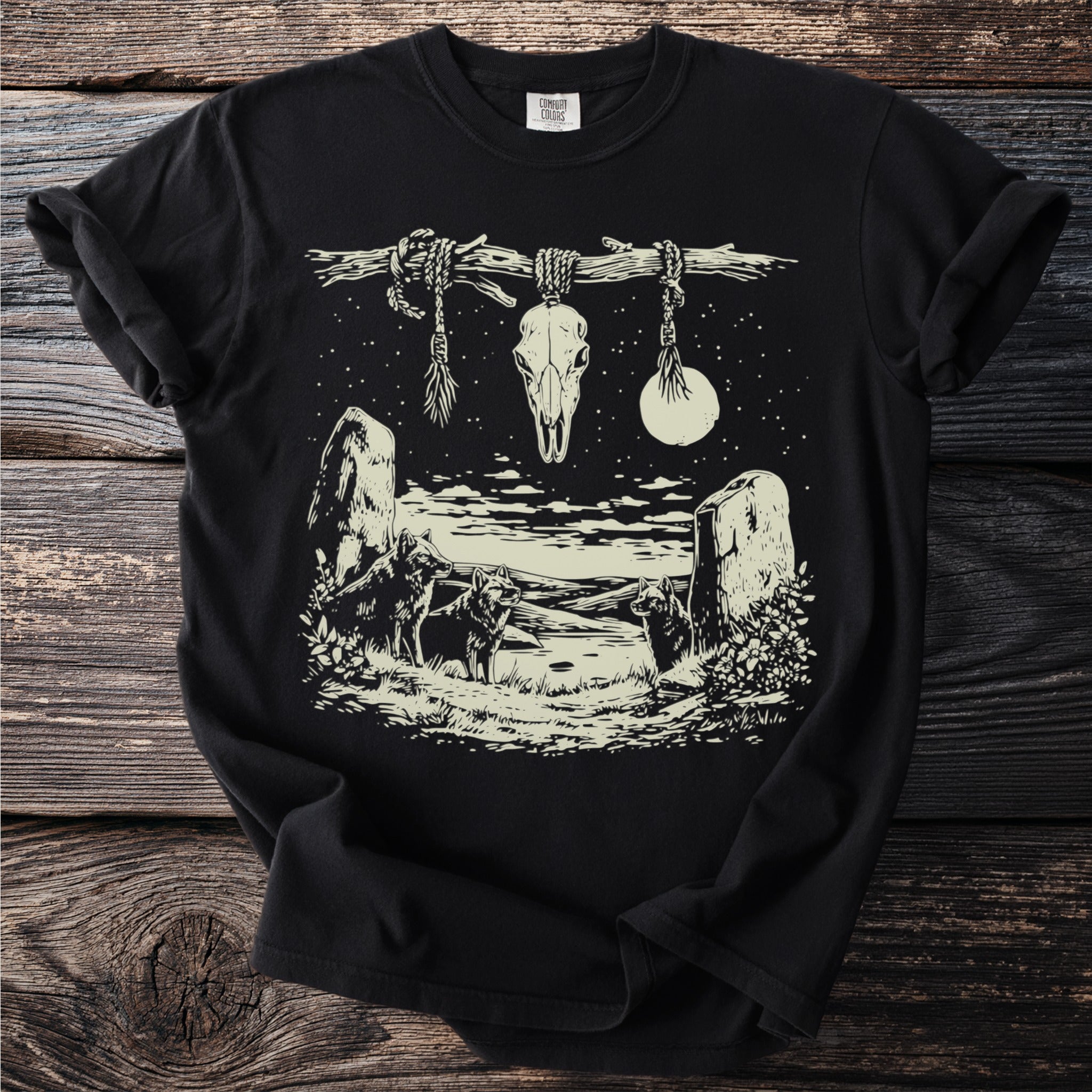 Black t-shirt with cream linework of wolves, rocks, moon, stars, and a skull hanging from a branch.