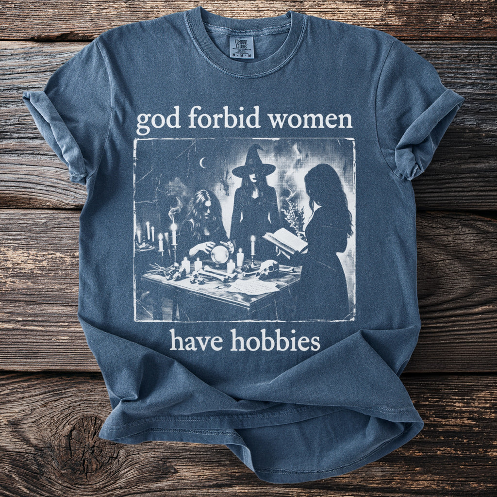 Blue t-shirt with "god forbid women have hobbies" and a witchy graphic.