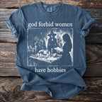 Blue t-shirt with "god forbid women have hobbies" and a witchy graphic.