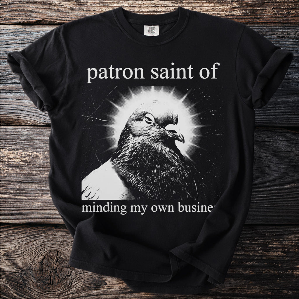Black t-shirt with a close-up of a pigeon and text "patron saint of minding my own business".