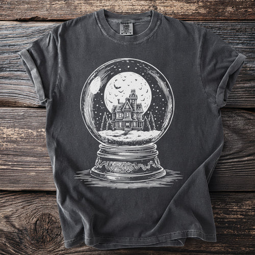 Dark t-shirt with white graphic of haunted house in a snow globe under a full moon.