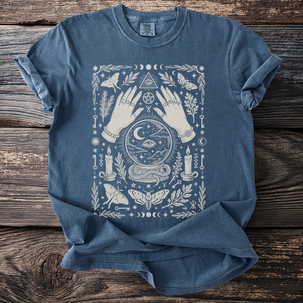 Blue t-shirt with occult graphic of hands, crystal ball, moths, candles, and celestial symbols.