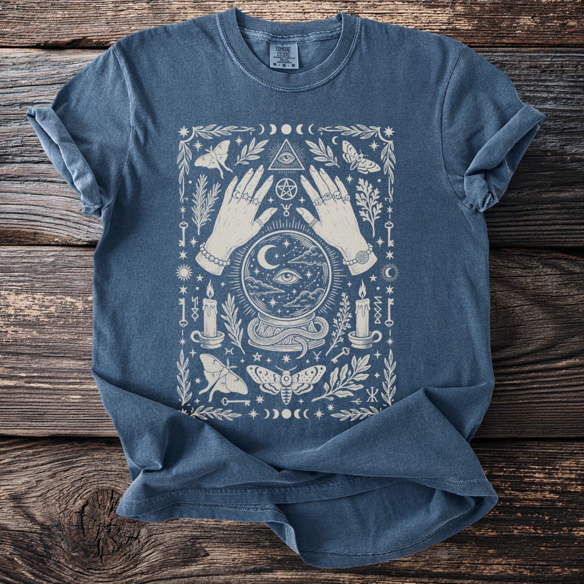 Blue t-shirt with occult graphic of hands, crystal ball, moths, candles, and celestial symbols.