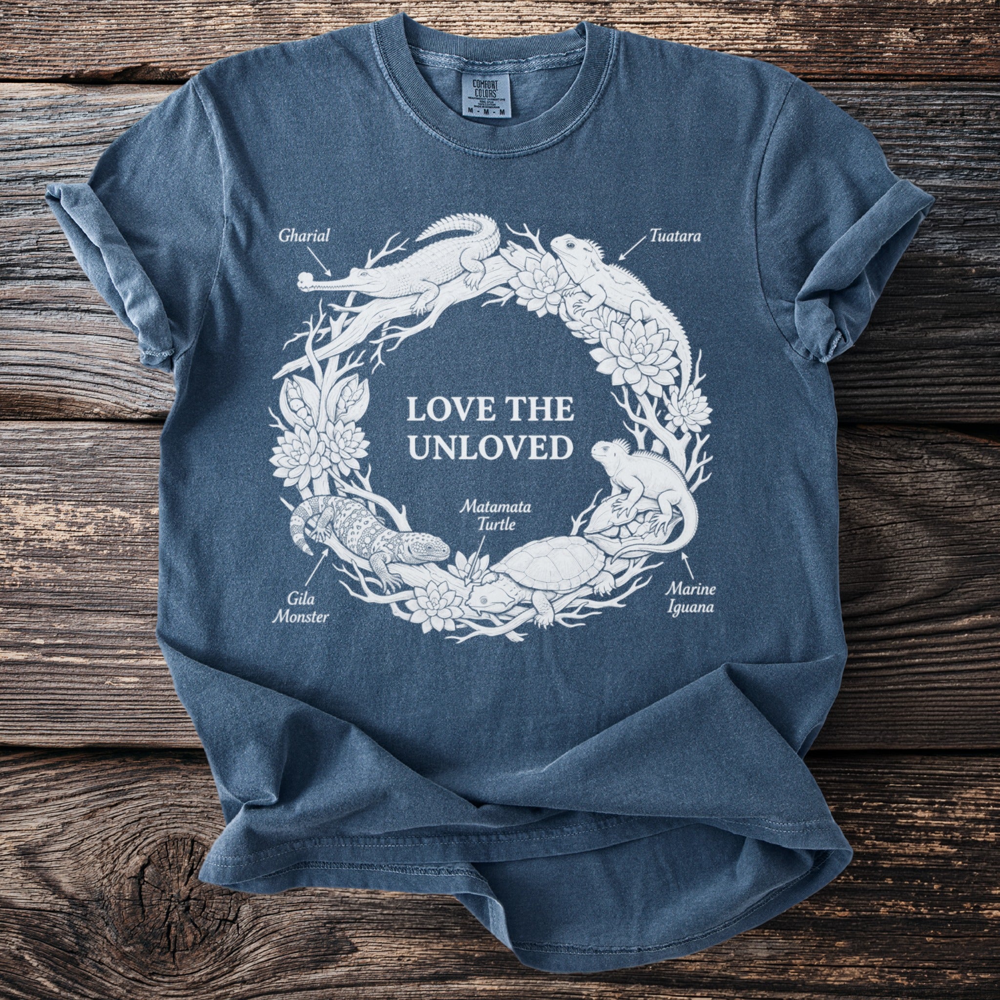 Blue t-shirt with white graphic of "Love the Unloved" text surrounded by reptiles and plants.