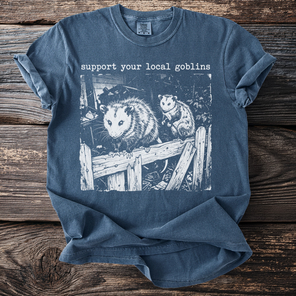 Blue t-shirt with two opossums on a wooden fence and text "support your local goblins".
