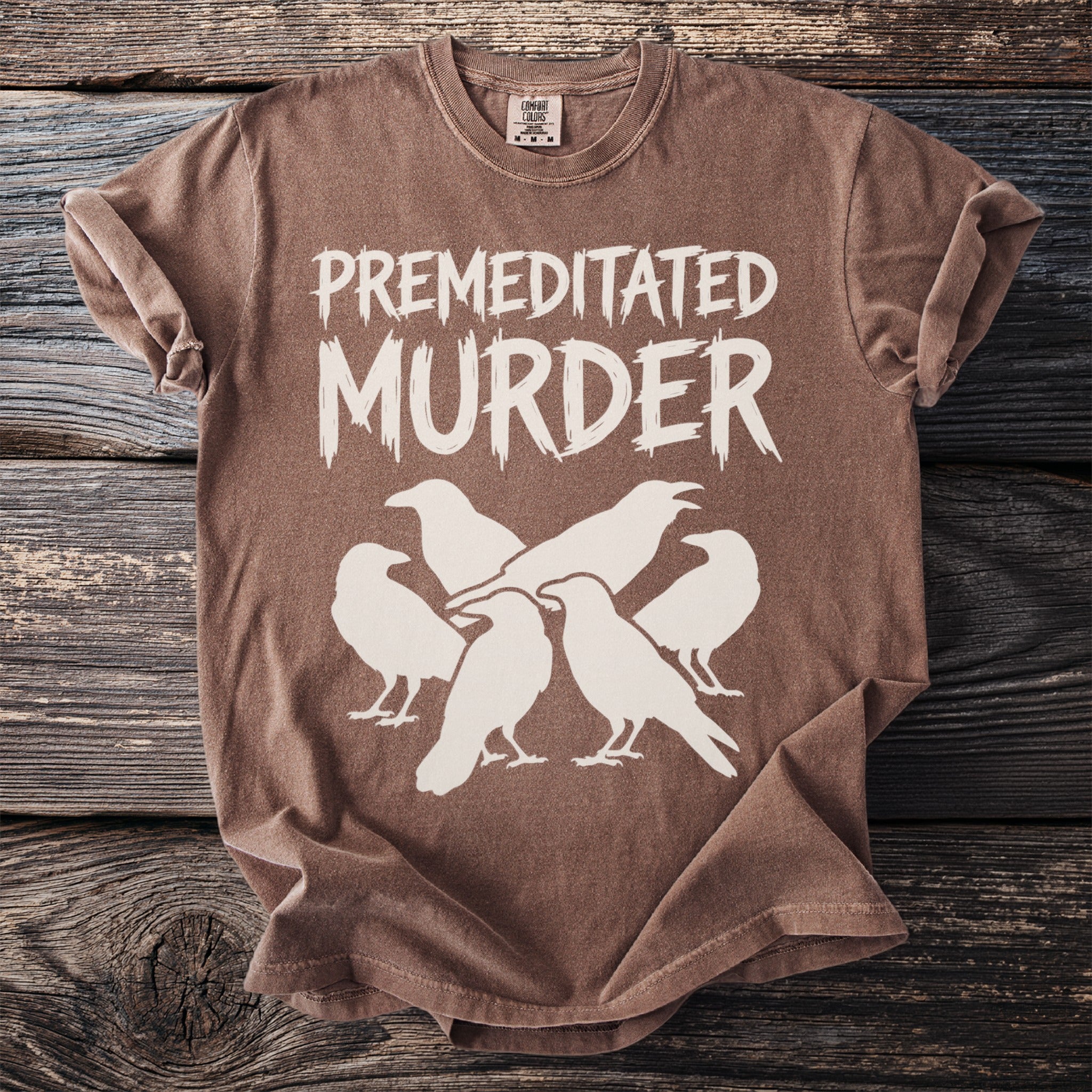 Brown t-shirt with white text "PREMEDITATED MURDER" above a flock of ravens.