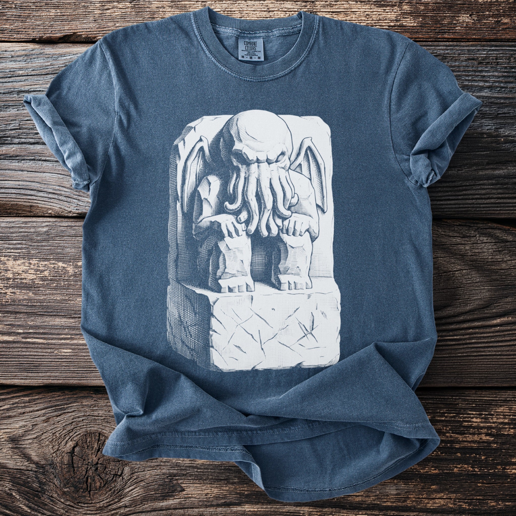 Blue t-shirt with a white, detailed illustration of a tentacled creature on a stone block.