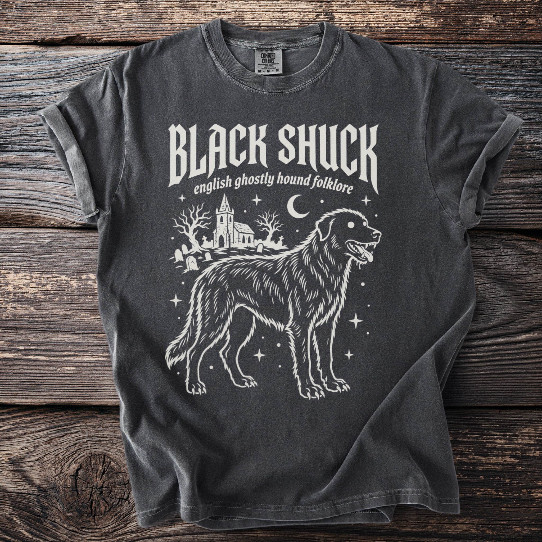 Dark gray t-shirt featuring a ghostly hound, graveyard, and church graphic with "BLACK SHUCK" text.