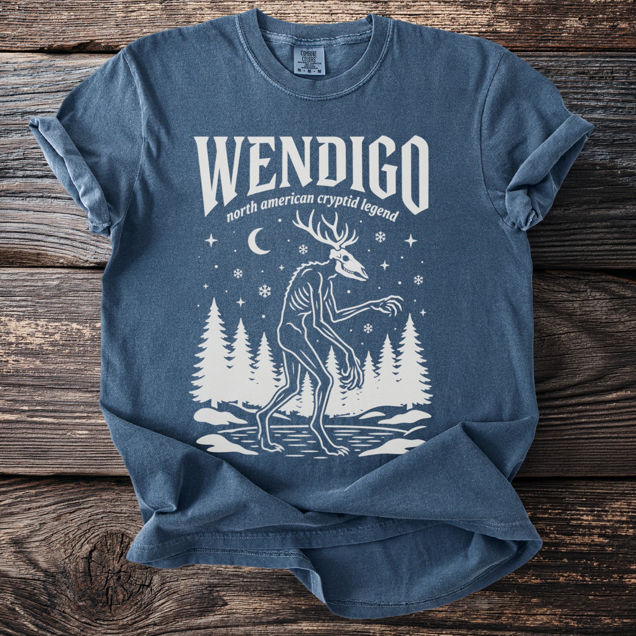 Blue t-shirt with white print of a Wendigo and forest scene.
