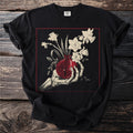 Skeleton hand holding a pomegranate with daffodils and leaves, on a black t-shirt.