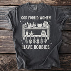 Dark gray t-shirt with white graphic of potions, crystals, and herbs, reading "God Forbid Women Have Hobbies."
