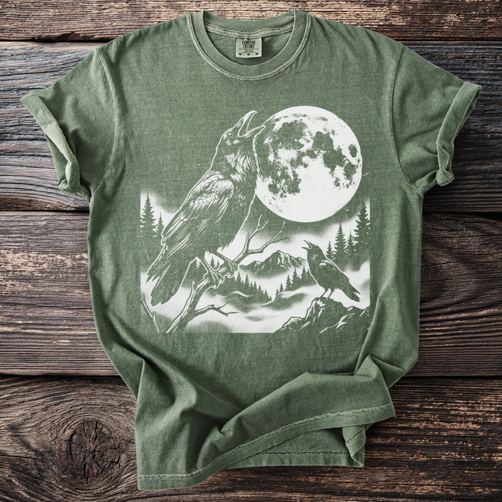 Green t-shirt with two ravens, full moon, and forest scene graphic.