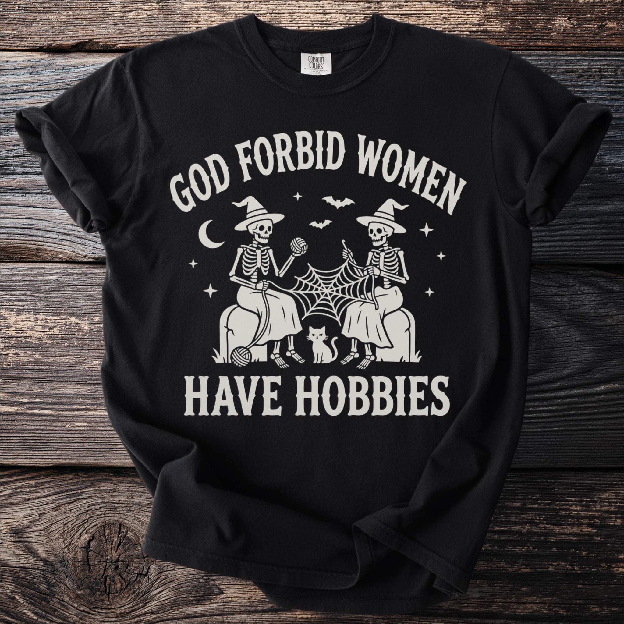 Black t-shirt with "God Forbid Women Have Hobbies" text and skeleton graphic.