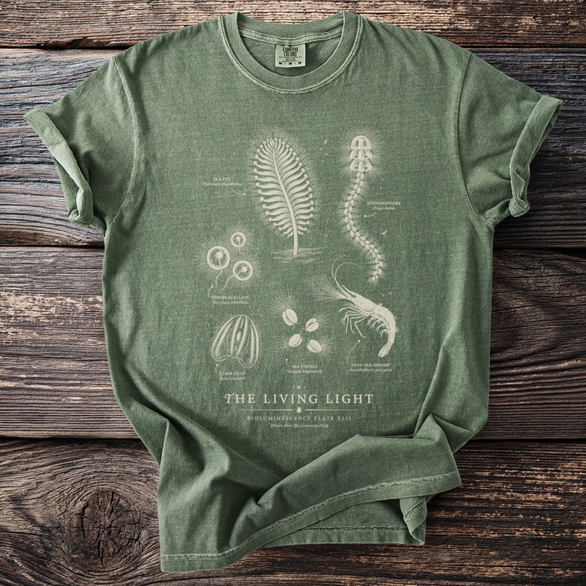Green t-shirt with "The Living Light Bioluminescence Plate XLII" design of sea creatures and text.