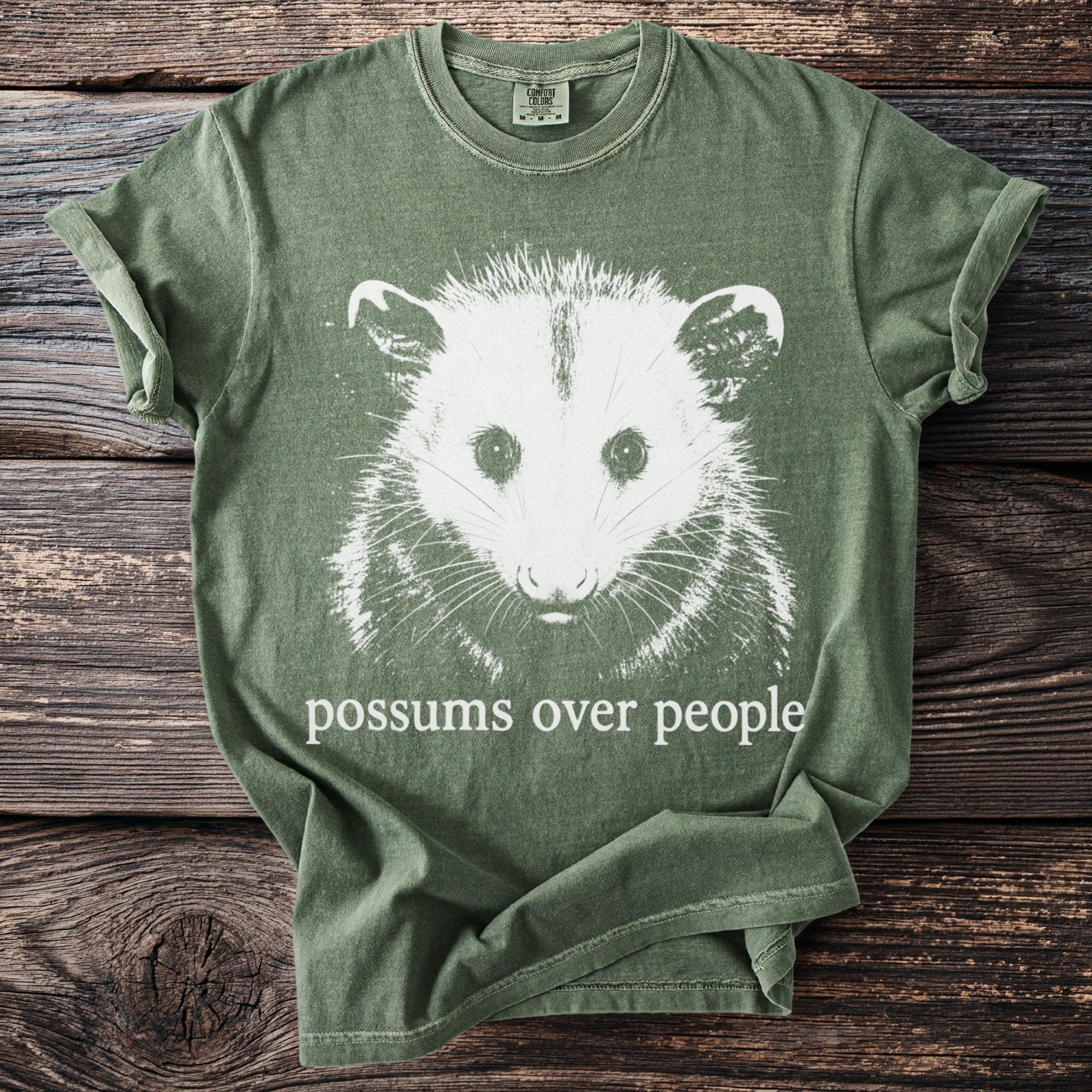 Green t-shirt with white possum graphic and text "possums over people".