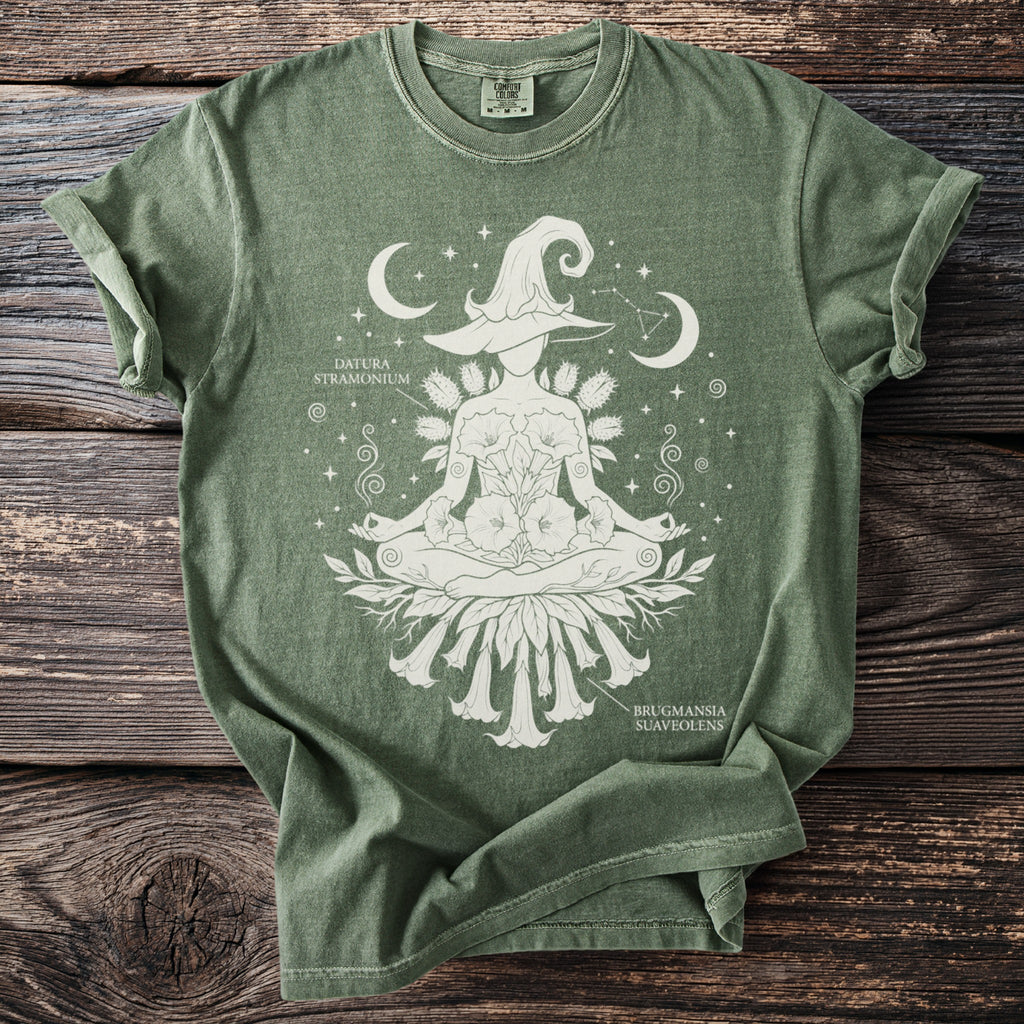 Green t-shirt with white screen print of a witch in lotus pose with botanical illustrations and celestial elements.