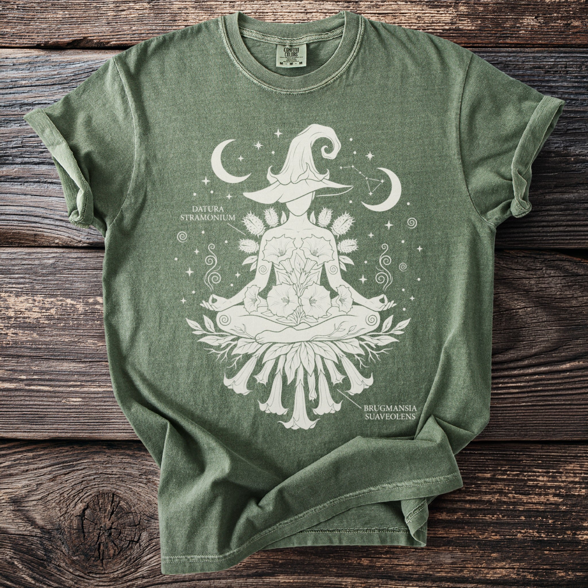Green t-shirt with white screen print of a witch in lotus pose with botanical illustrations and celestial elements.
