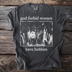 Dark grey t-shirt with "God forbid women have hobbies" and a graveyard scene with witches.