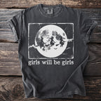 Dark grey t-shirt with graphic of three witches flying in front of a moon and text "girls will be girls."