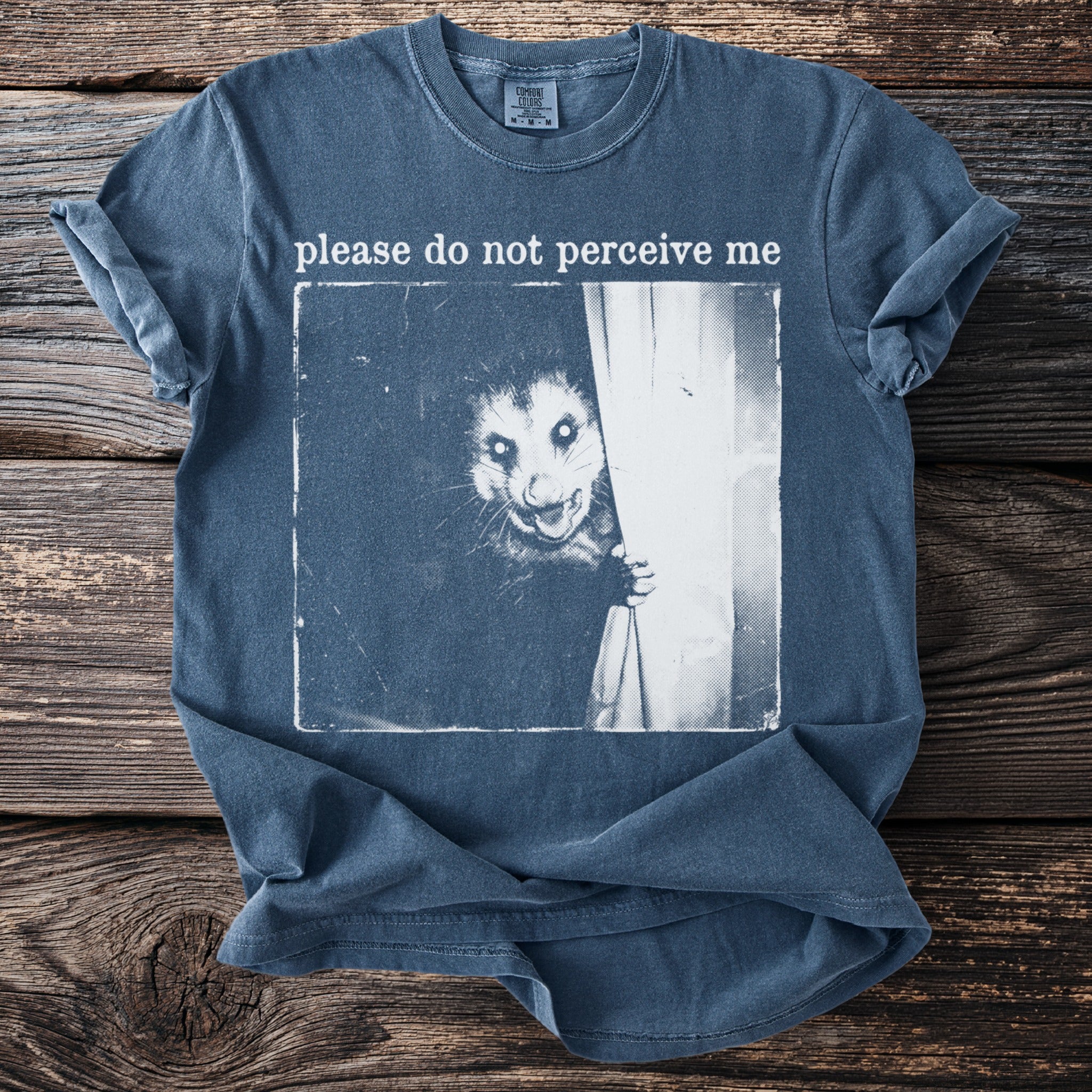 Blue t-shirt with a black and white opossum peeking from behind a curtain and text.