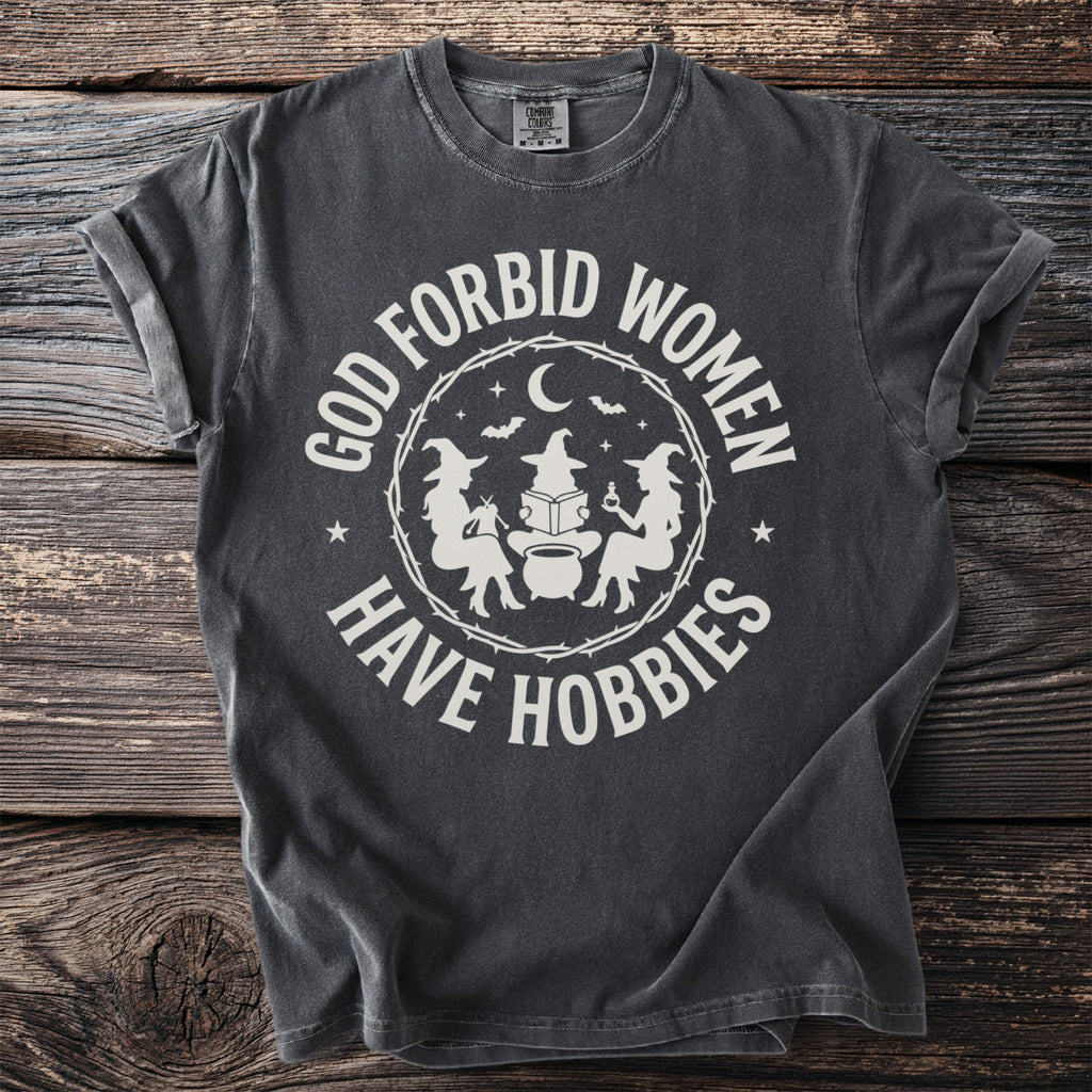 Dark gray t-shirt with white text "GOD FORBID WOMEN HAVE HOBBIES" and witch graphics.
