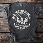 Dark gray t-shirt with white text "GOD FORBID WOMEN HAVE HOBBIES" and witch graphics.