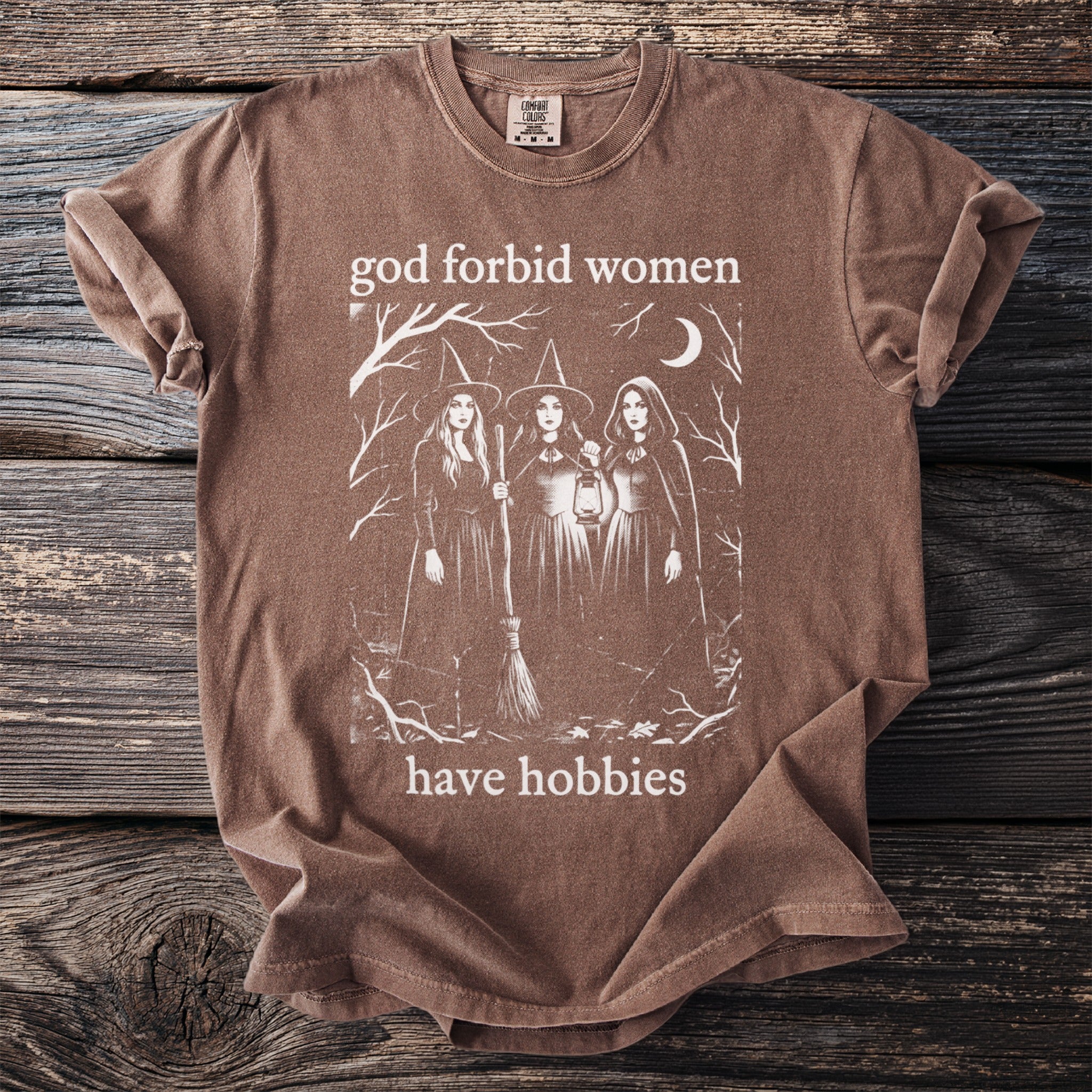 Brown t-shirt with three witches and text "god forbid women have hobbies".